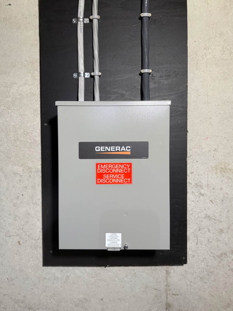 Generac 100-amp emergency disconnect and transfer switch mounted on a basement backboard