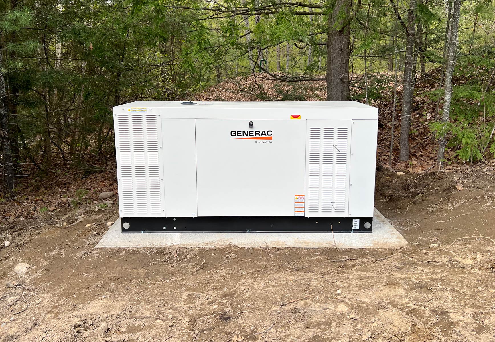 Generac Protector 60kW liquid-cooled standby generator on a concrete pad in a wooded New Hampshire setting