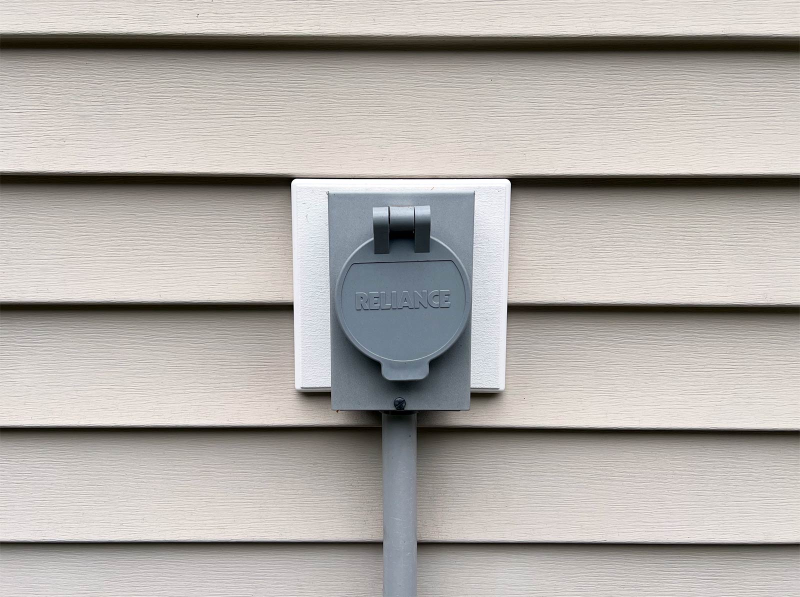 Weatherproof portable generator inlet box with a hinged cover mounted on the siding of a home, conduit running down to the panel