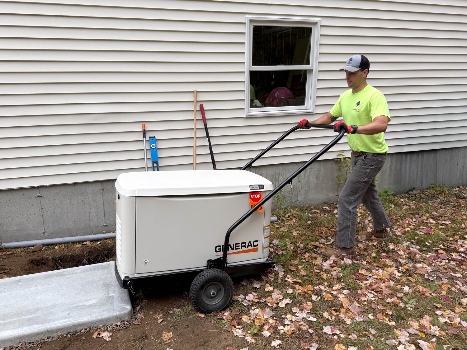 Michael Stacey of Upright Electric rolling a Generac standby generator onto a concrete pad beside a New Hampshire home