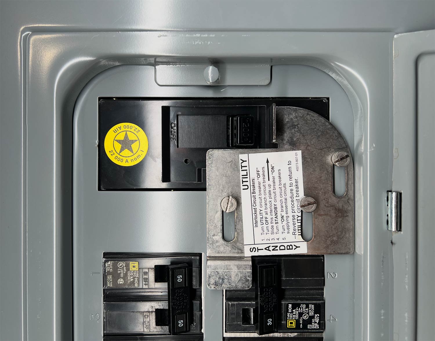Close-up of a generator interlock plate over the main and standby breakers in a residential panel, with the utility and standby switching steps printed on it