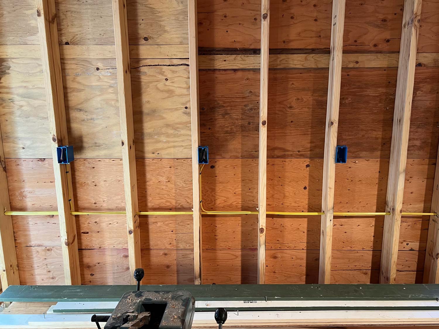 Yellow cable and three blue outlet boxes stapled to wood studs during a new-construction rough-in