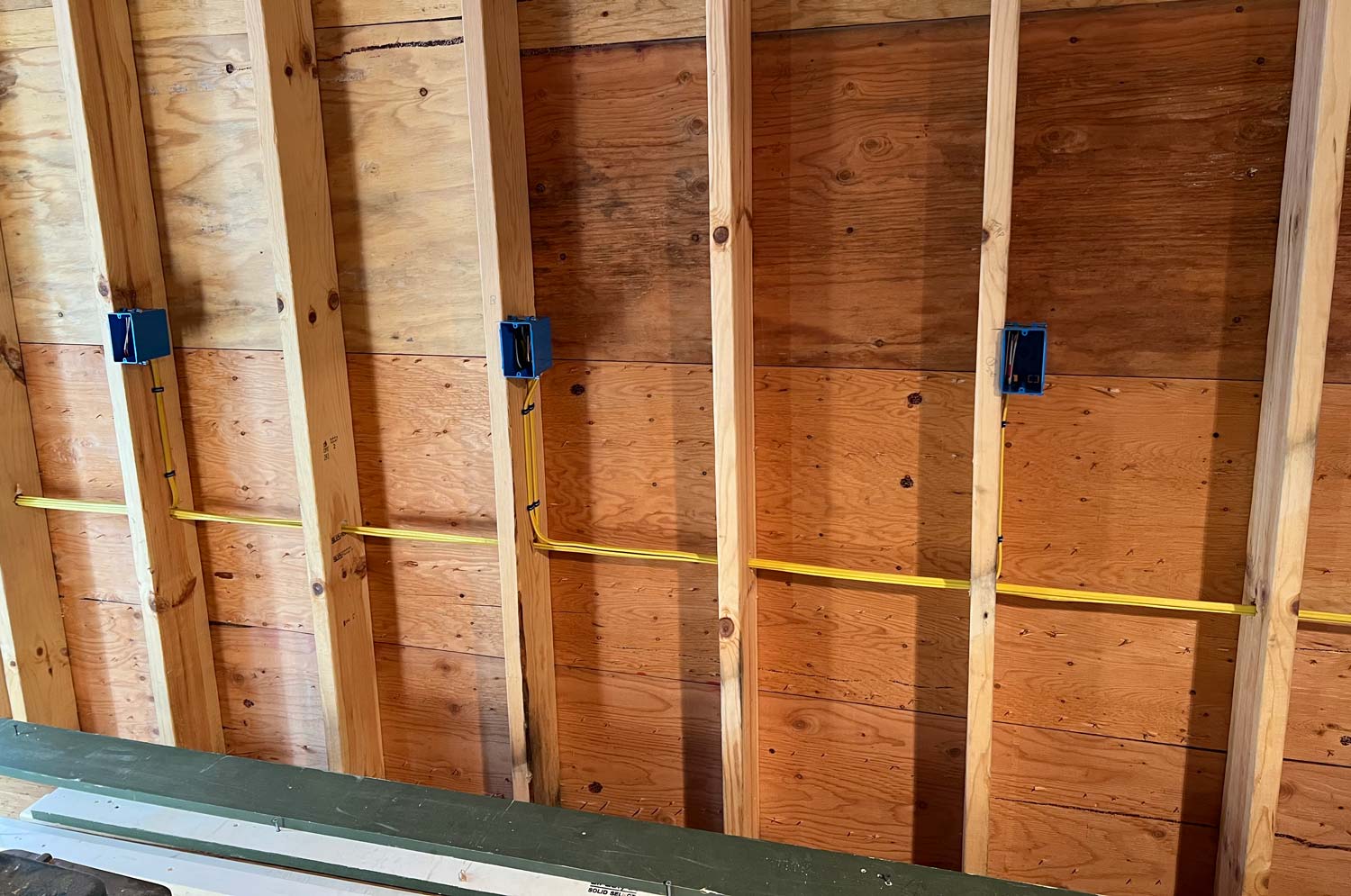 Yellow cable and blue outlet boxes stapled to wood studs during a new-construction rough-in