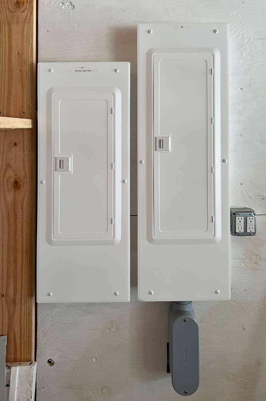 New main electrical panel and a critical load subpanel mounted side by side on a white wall