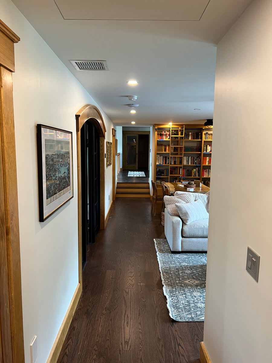 Recessed can lights in a straight run down a hallway with hardwood floors and a two-gang switch in the foreground
