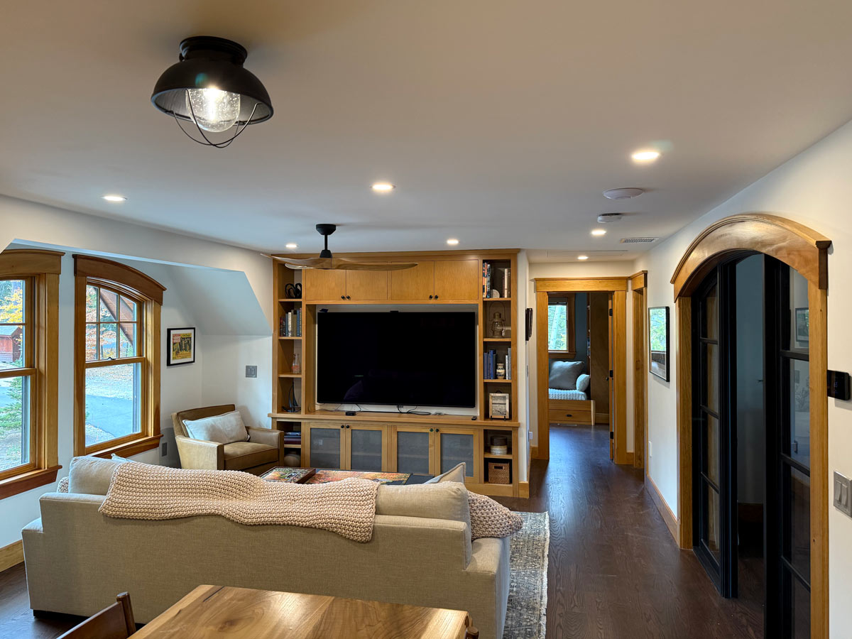 Living room with a caged flush-mount fixture, recessed LED cans, a ceiling fan, and a wall-mounted TV in a wood built-in