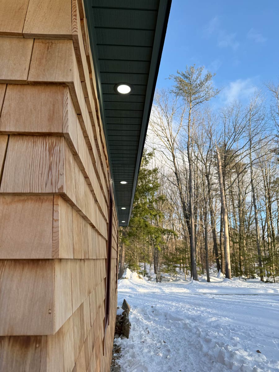 Recessed LED soffit lights running along the eave of a cedar shingle home in winter