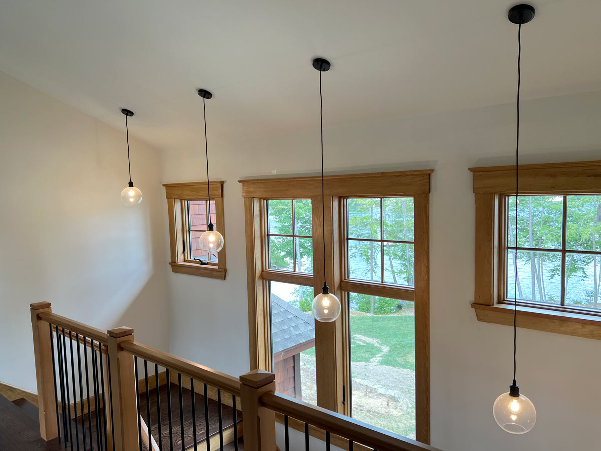 Four glass globe pendants hanging at staggered lengths over a stairwell with lake views through wood-framed windows