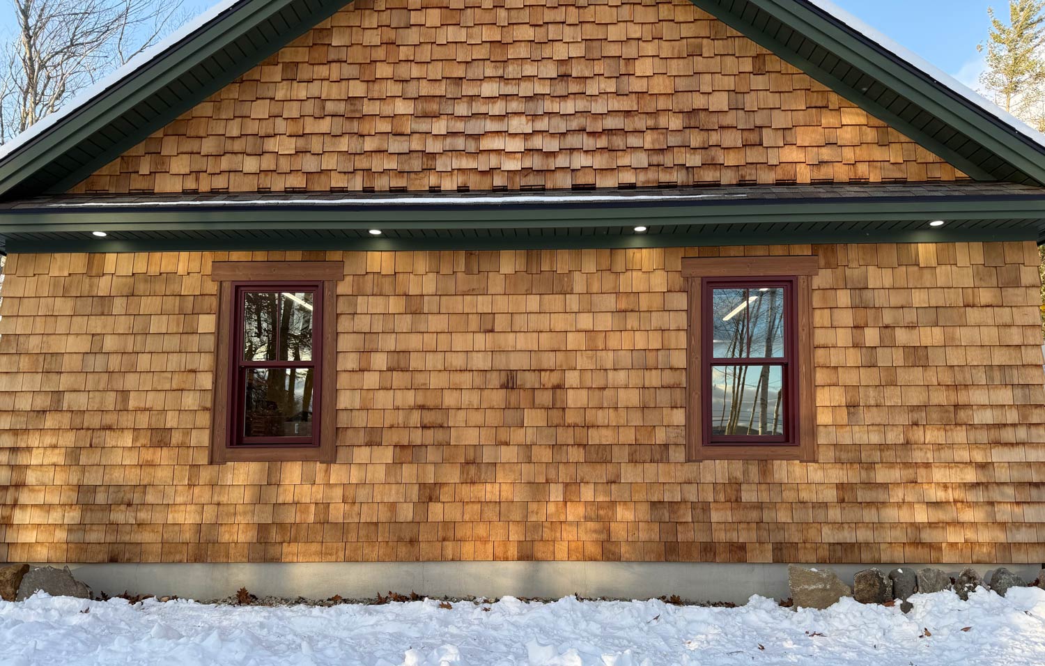 Cedar shingle home in Sandwich, NH with recessed soffit lights along the eave and snow on the ground